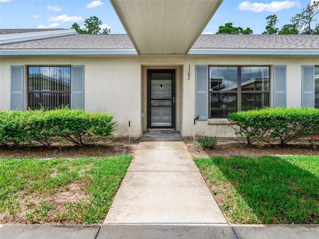 A concrete walkway leads to the front door of a single-story house with shutters — 1701 SE 24TH ROAD UNIT 1702, OCALA, FL