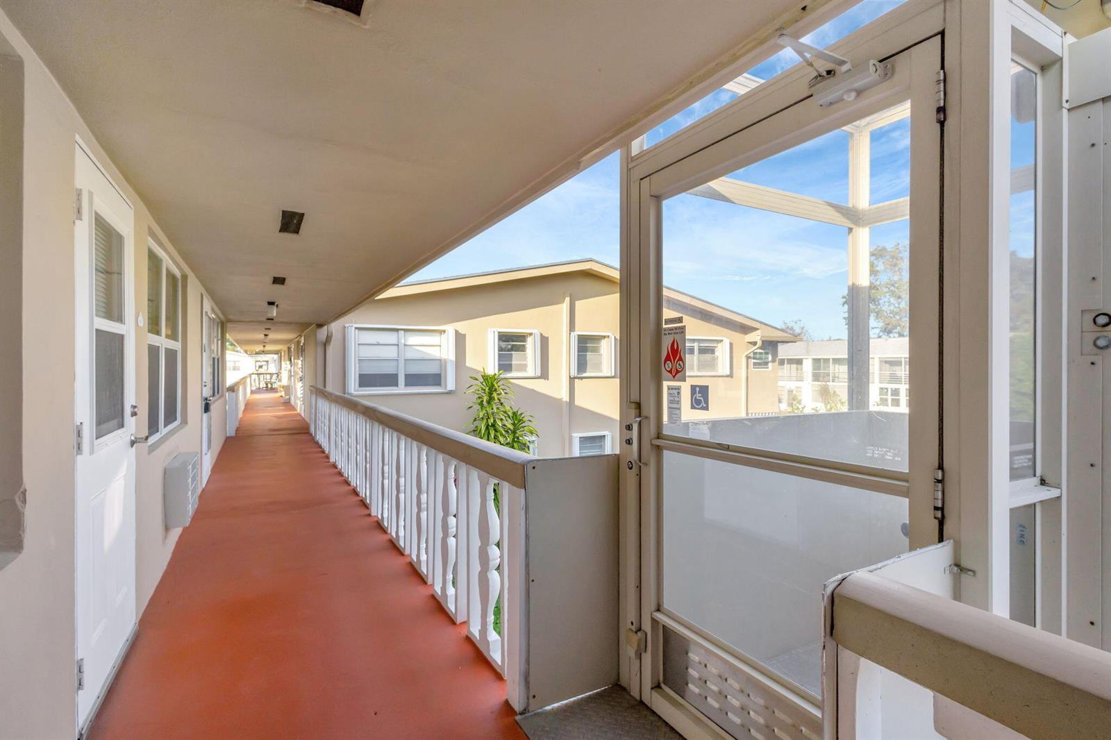 An outdoor walkway with a red floor and white railing leads past apartment doors — 121 Bedford E, West Palm Beach FL 33417, WEST PALM BEACH, FL