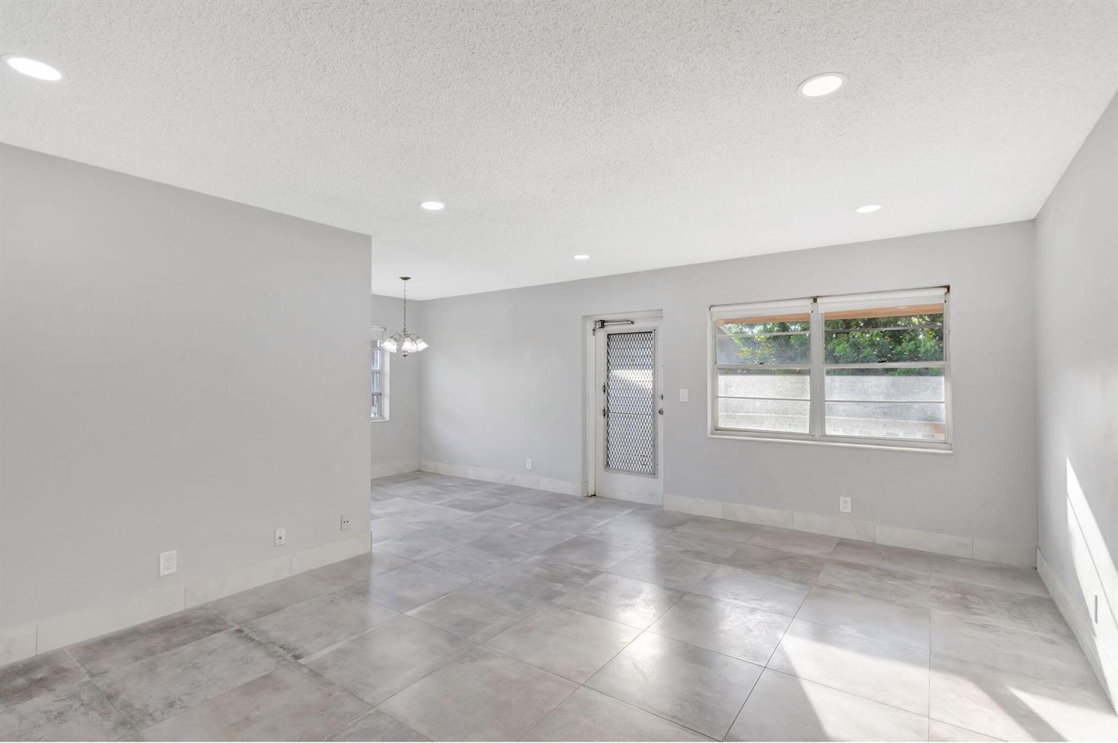 An empty room with gray tile flooring, light gray walls, recessed lighting, and a glass door — 121 Bedford E, West Palm Beach FL 33417, WEST PALM BEACH, FL