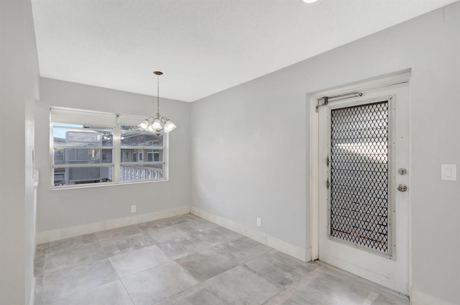 A dining area with gray tile flooring, light gray walls, a chandelier, and a screen door — 121 Bedford E, West Palm Beach FL 33417, WEST PALM BEACH, FL