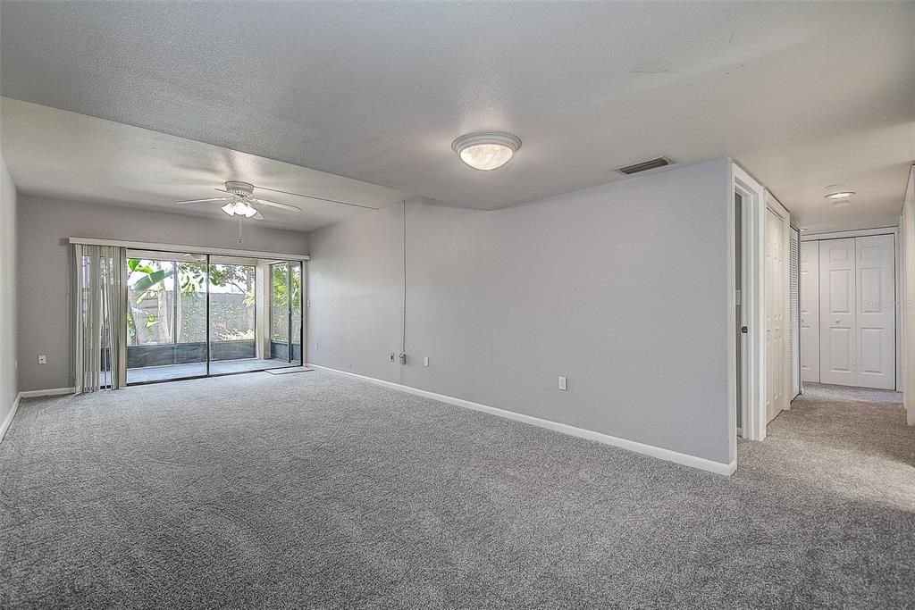 A spacious living room features gray carpeting, light gray walls, and sliding glass patio doors — 860 S VILLAGE DRIVE N UNIT 106, ST PETERSBURG, FL