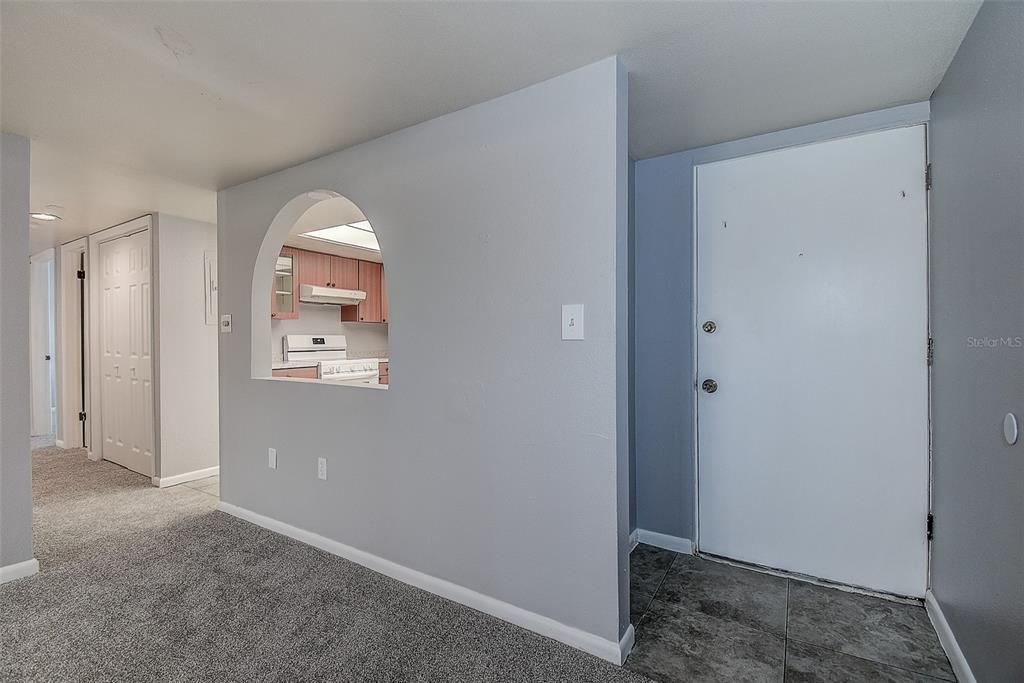An entryway with a tiled floor leads to a carpeted living area with a kitchen pass-through — 860 S VILLAGE DRIVE N UNIT 106, ST PETERSBURG, FL