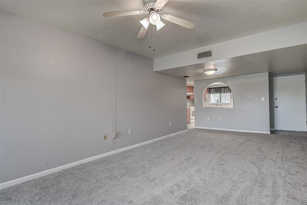 A carpeted living room features a ceiling fan, a pass-through window, and a white door — 860 S VILLAGE DRIVE N UNIT 106, ST PETERSBURG, FL