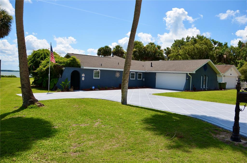 A blue single-story house with a white garage door and a patterned concrete driveway — 1102 N PALMETTO STREET, LEESBURG, FL