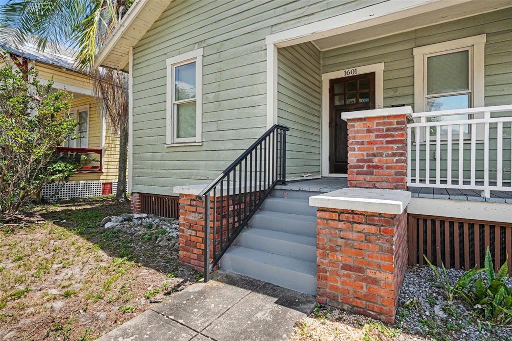 The exterior of a light green house features a brick-based porch with a black railing — 1601 E 15TH AVENUE, TAMPA, FL