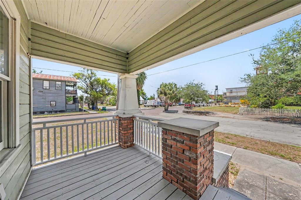 A covered front porch with gray wooden decking, brick pillars, and white railings — 1601 E 15TH AVENUE, TAMPA, FL