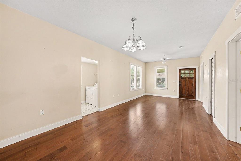 An empty living room features hardwood floors, a chandelier, and a doorway to a laundry area — 1601 E 15TH AVENUE, TAMPA, FL