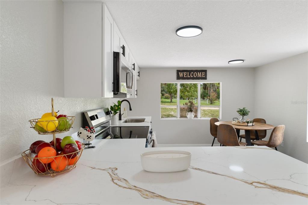 A kitchen with white cabinets and quartz countertops overlooks a dining area with a window — 3320 N HOLIDAY DRIVE, CRYSTAL RIVER, FL
