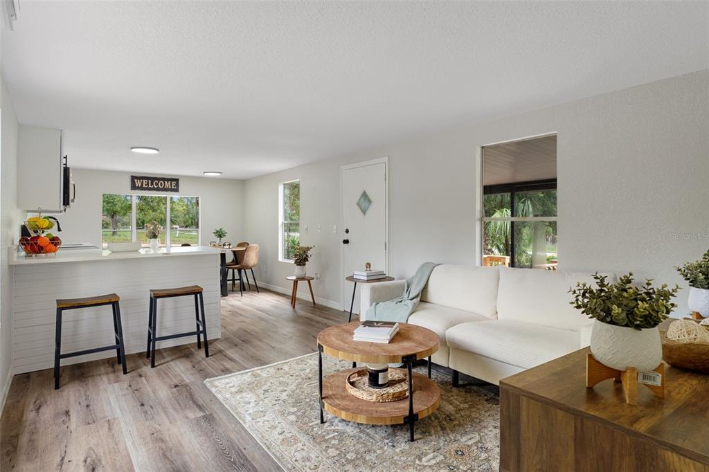 A bright living room and kitchen area features wood-look flooring, white walls, and neutral furniture — 3320 N HOLIDAY DRIVE, CRYSTAL RIVER, FL