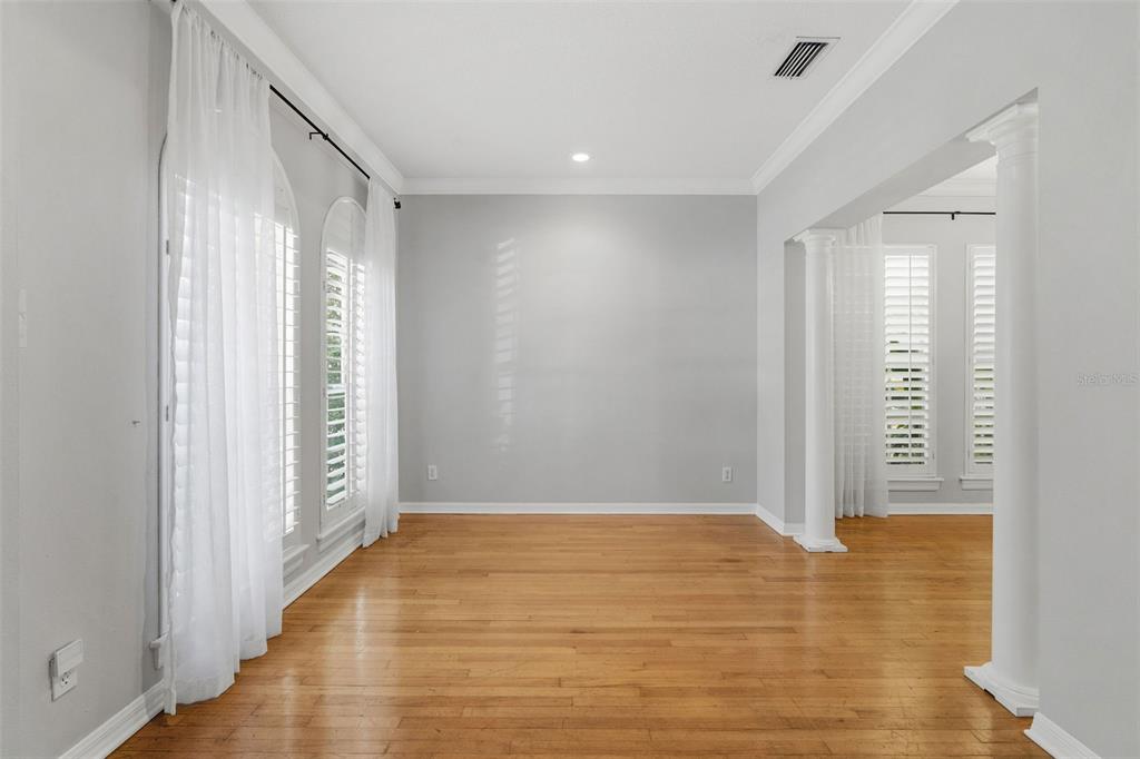 An empty room with hardwood floors, white walls, arched windows with curtains, and decorative columns — 3710 W LEONA STREET, TAMPA, FL