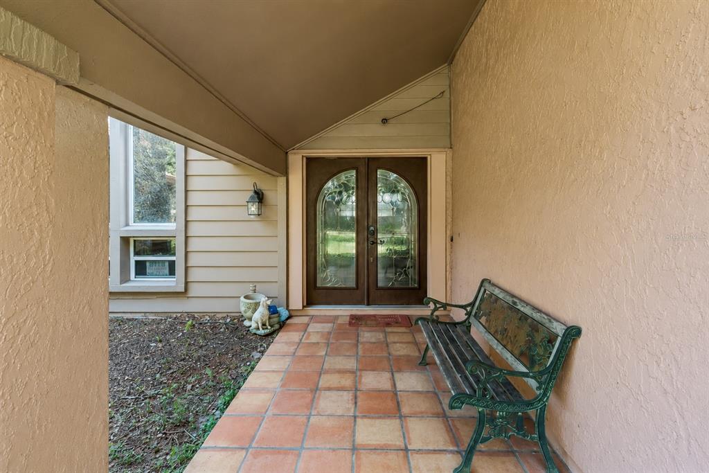 A covered front porch features a tiled floor, a metal bench, and double glass doors — 5405 BAYBROOK AVENUE, ORLANDO, FL