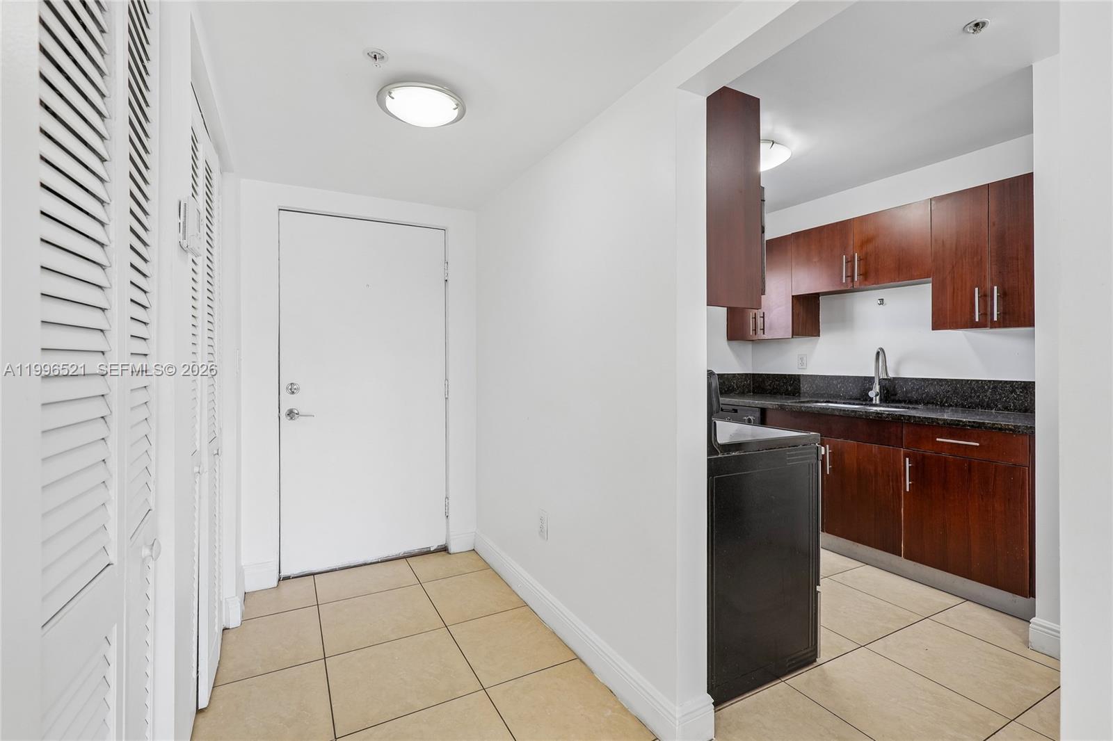 A white entryway leads to a kitchen with dark wood cabinets and granite countertops — 4137 Stirling Rd # 507, Dania Beach FL 33314, DANIA BEACH, FL