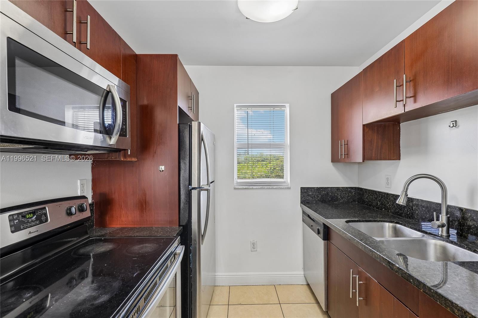 A galley kitchen features dark wood cabinets, black granite countertops, and stainless steel appliances — 4137 Stirling Rd # 507, Dania Beach FL 33314, DANIA BEACH, FL