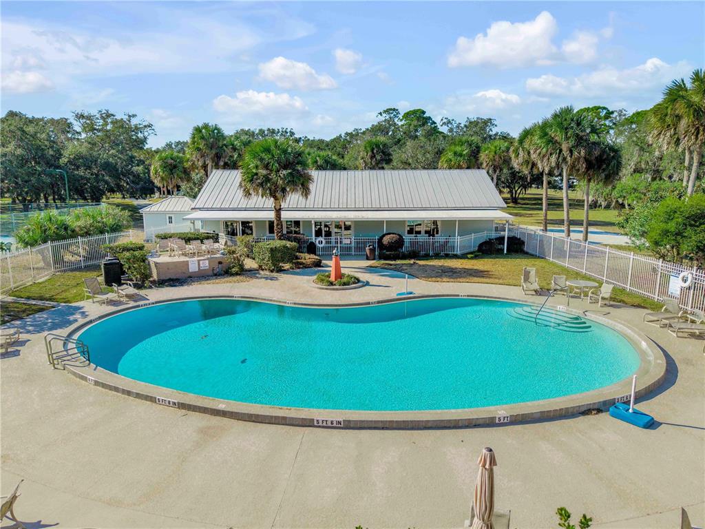 An outdoor swimming pool with a clubhouse and palm trees in a residential setting — 317 WATER LANDING DRIVE, OAK HILL, FL