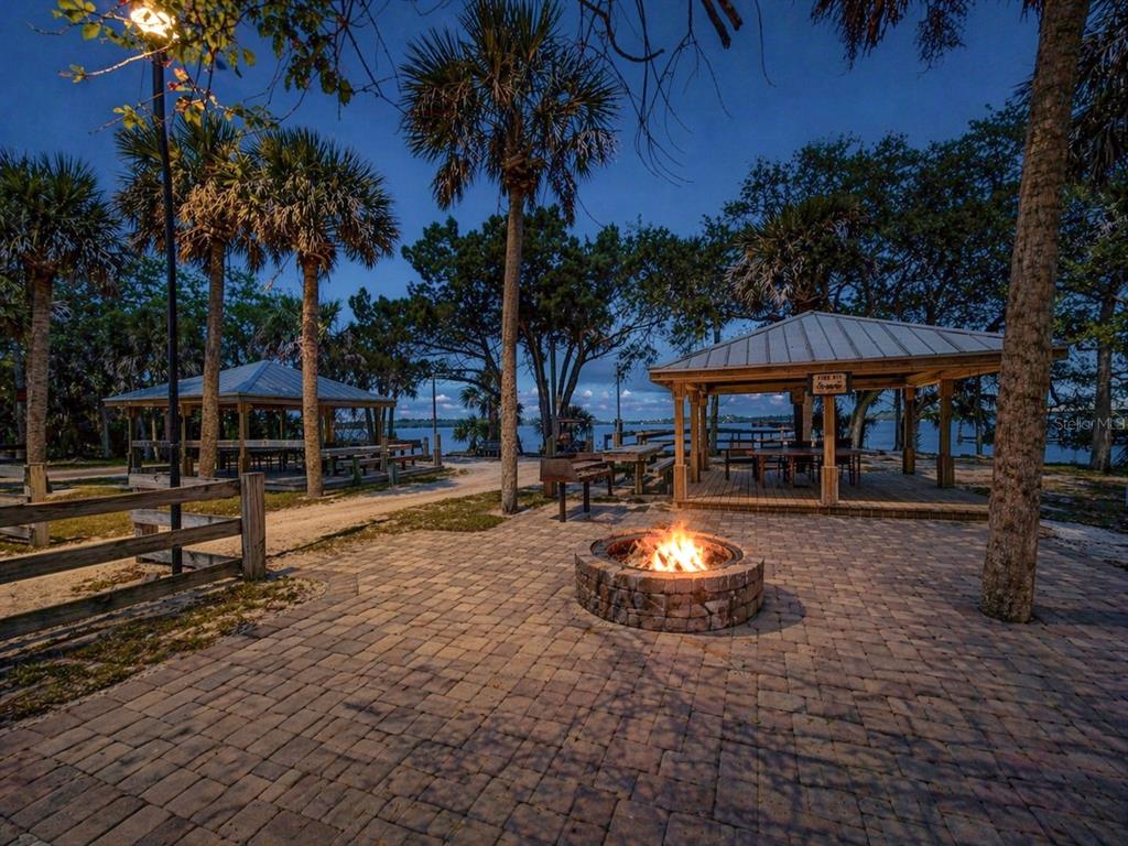A stone fire pit sits on a paved patio near two gazebos overlooking a lake — 317 WATER LANDING DRIVE, OAK HILL, FL