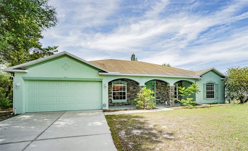 A single-story house with light green stucco, a stone facade, and an attached two-car garage — 6283 LORRAINE LANE, SPRING HILL, FL