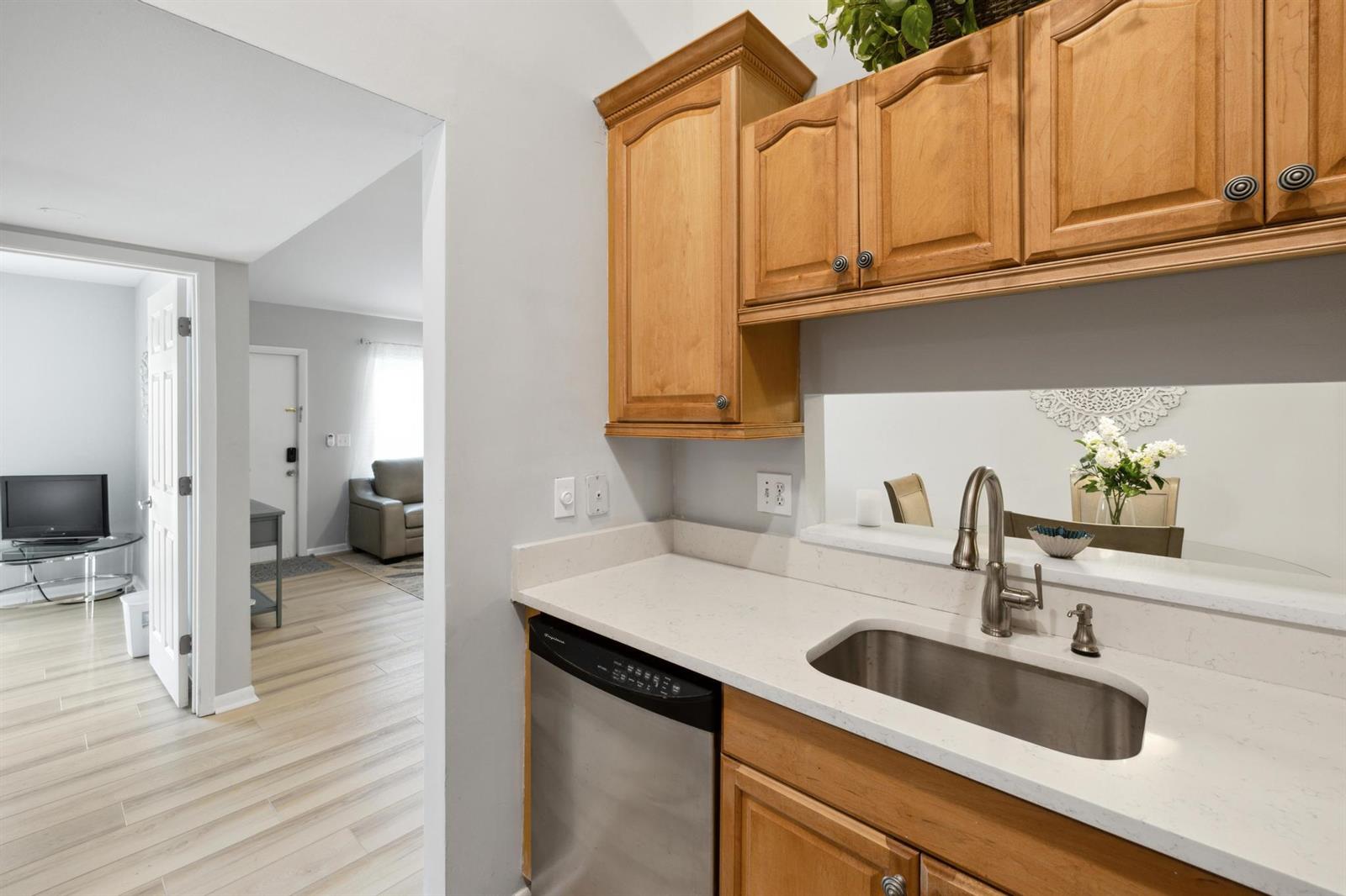 A kitchen sink and dishwasher are set into a white countertop beneath wooden cabinets — 6271 Chasewood Drive # F, Jupiter FL 33458, JUPITER, FL