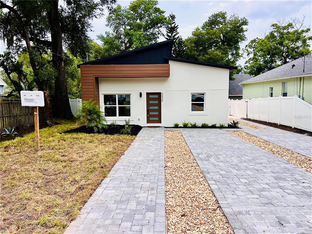 A modern, single-story house features a white stucco exterior, wood-paneled accent, and a paved driveway — 5808 N 16TH STREET, TAMPA, FL