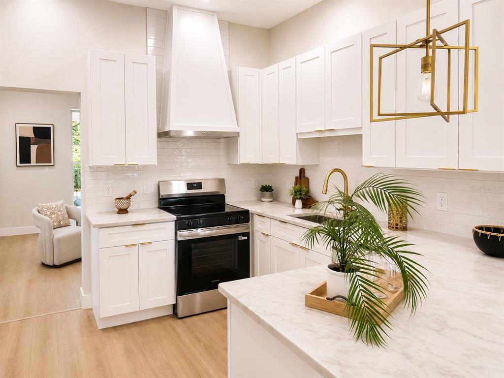 A modern kitchen features white cabinets, marble countertops, stainless steel appliances, and a gold pendant light — 5808 N 16TH STREET, TAMPA, FL