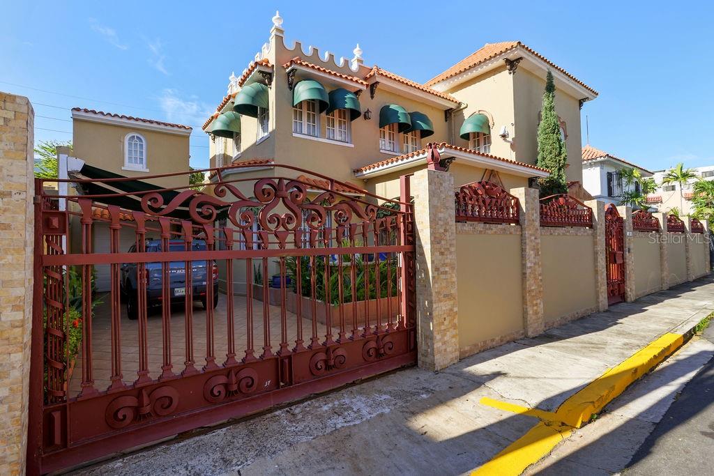 A two-story tan house with green awnings sits behind a decorative red metal gate — 1404 VILA MAYO, SAN JUAN, PR