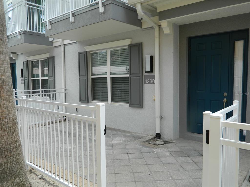 A gray townhome exterior features a blue front door, white fencing, and a paved patio — 1330 BOLTON PLACE, LAKE MARY, FL
