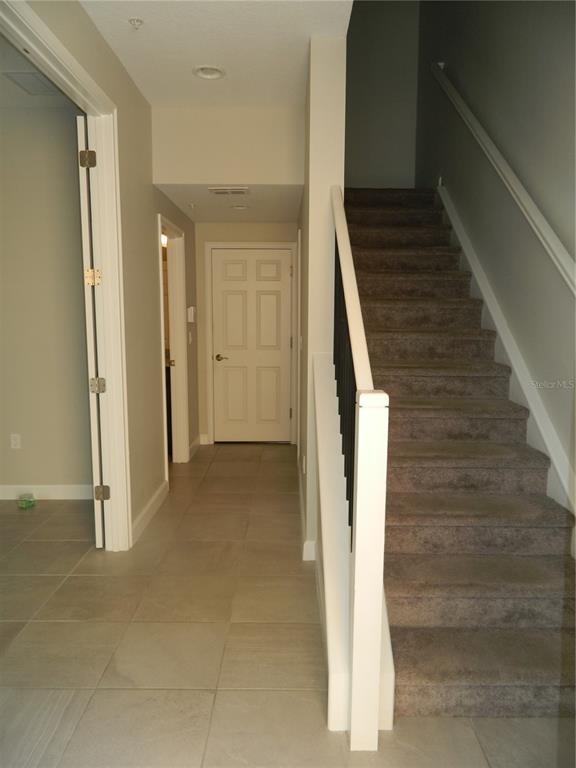 A hallway with tile flooring leads to a closed door beside a carpeted staircase — 1330 BOLTON PLACE, LAKE MARY, FL