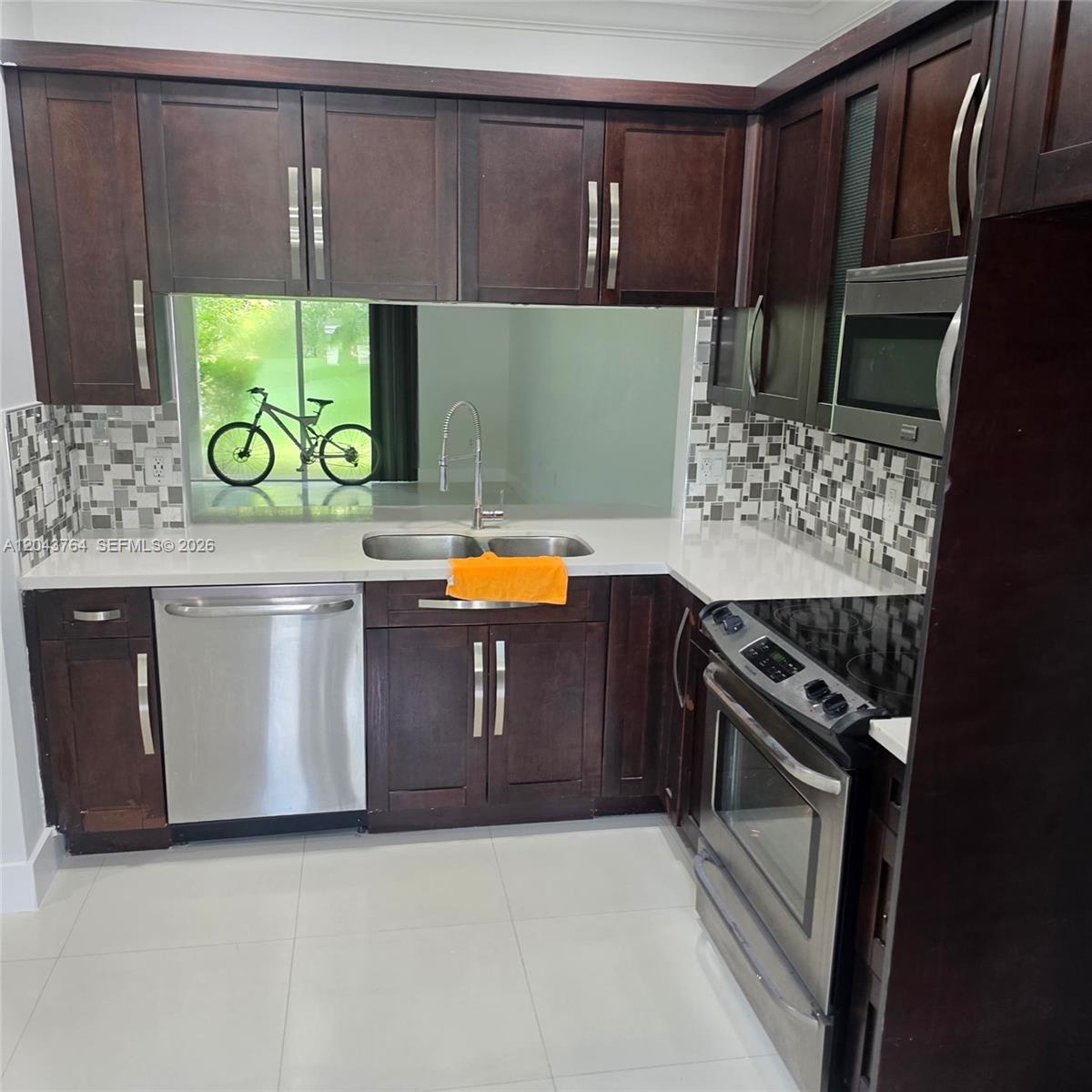 A kitchen features dark wood cabinets, stainless steel appliances, white countertops, and a mosaic backsplash — 8215 SW 27th St # 103, Miramar FL 33025, MIRAMAR, FL