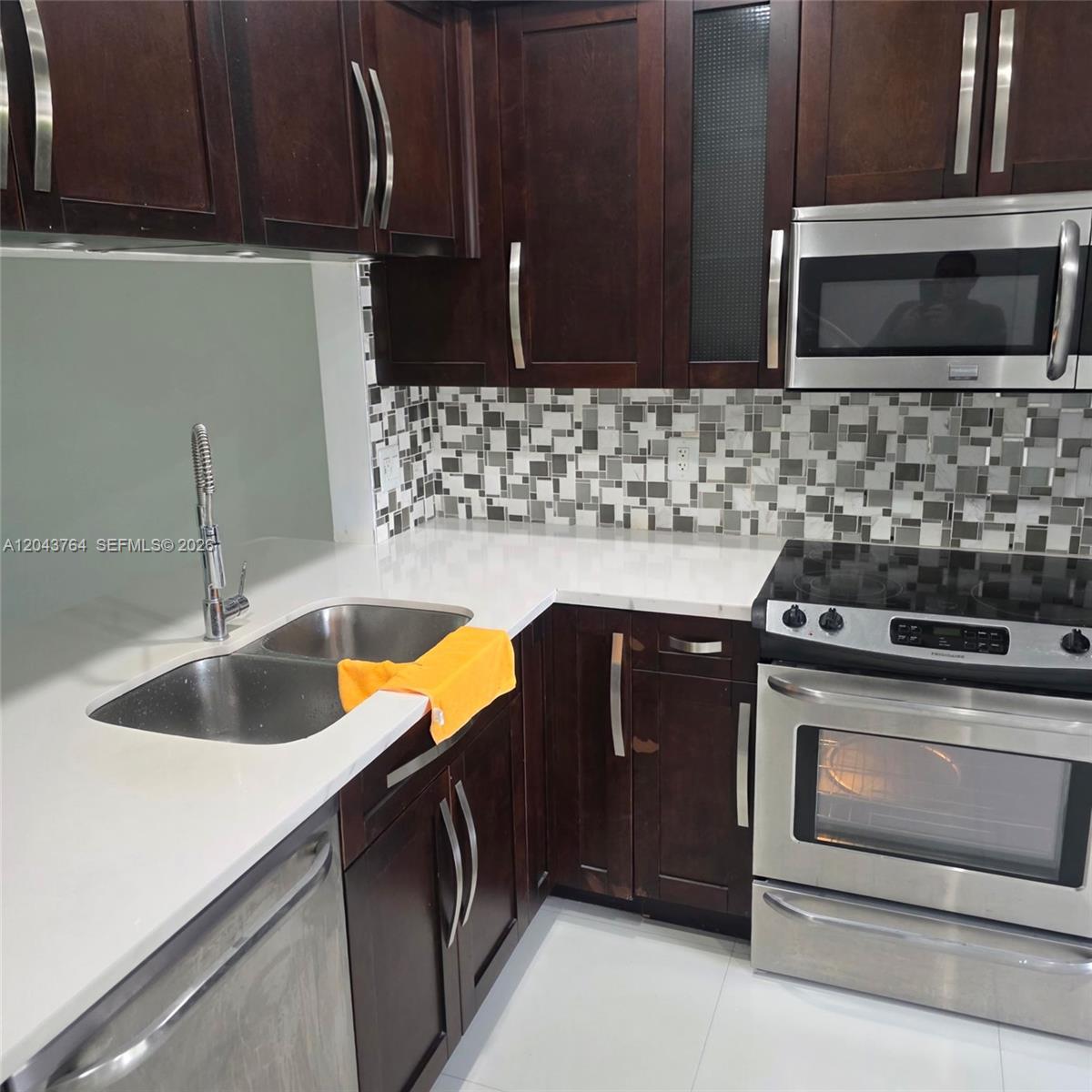 A kitchen features dark wood cabinets, stainless steel appliances, and a mosaic tile backsplash — 8215 SW 27th St # 103, Miramar FL 33025, MIRAMAR, FL
