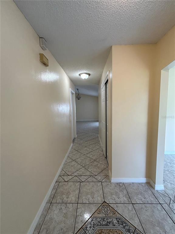 A hallway with light-colored tile flooring leads to an open living area with a chandelier — 1090 JASON RIDGE COURT, KISSIMMEE, FL