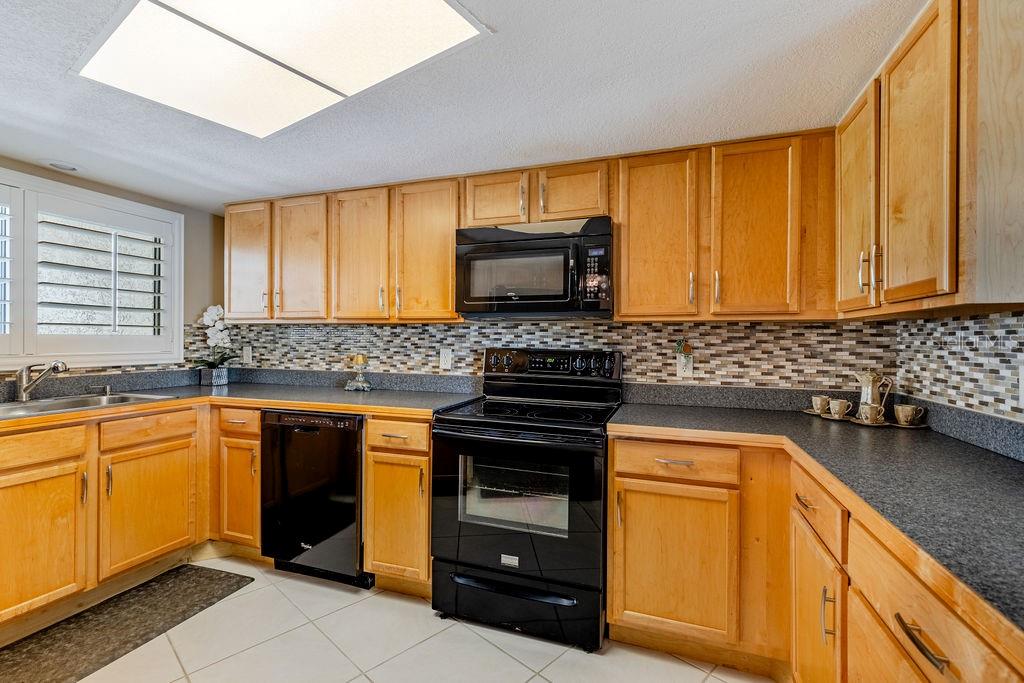 A kitchen features light wood cabinets, black appliances, dark countertops, and a mosaic tile backsplash — 1068 LOTUS PARKWAY UNIT 813, ALTAMONTE SPRINGS, FL