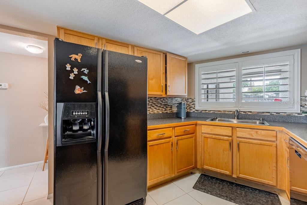 A kitchen with light wood cabinets, a black refrigerator, and a tiled backsplash — 1068 LOTUS PARKWAY UNIT 813, ALTAMONTE SPRINGS, FL