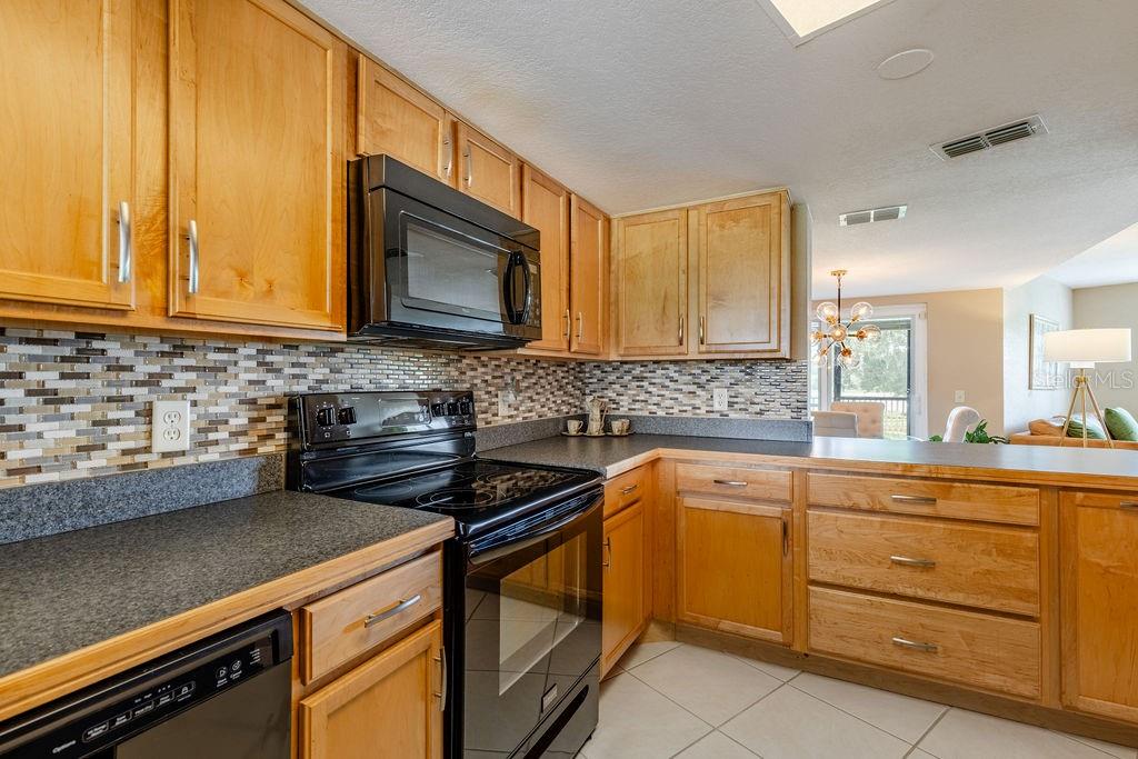 A kitchen features wood cabinets, black appliances, a mosaic tile backsplash, and dark countertops — 1068 LOTUS PARKWAY UNIT 813, ALTAMONTE SPRINGS, FL