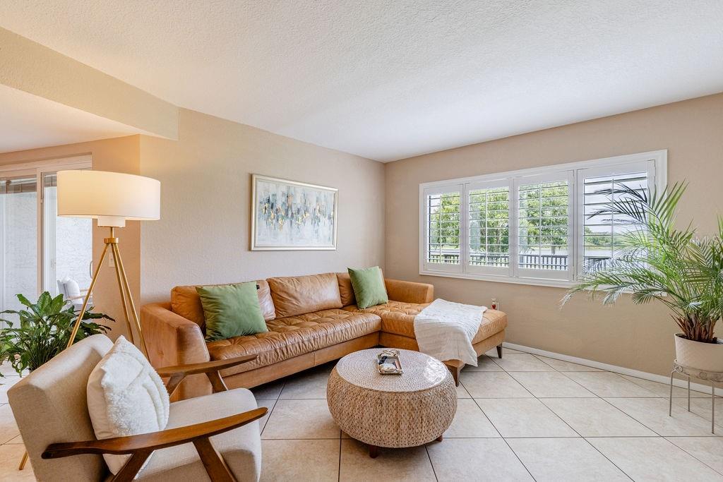 A living room features a tan leather sectional, a round woven coffee table, and plantation shutters — 1068 LOTUS PARKWAY UNIT 813, ALTAMONTE SPRINGS, FL