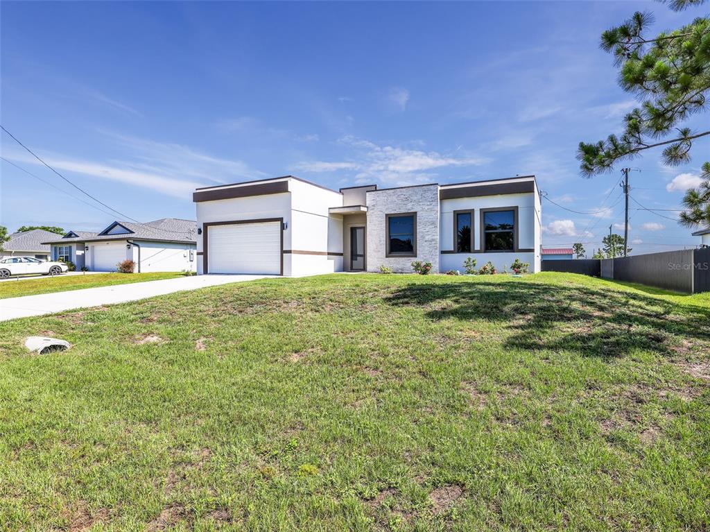 A modern, single-story house with a white exterior, stone accent wall, and a one-car garage — 1423 NW 20TH TERRACE, CAPE CORAL, FL