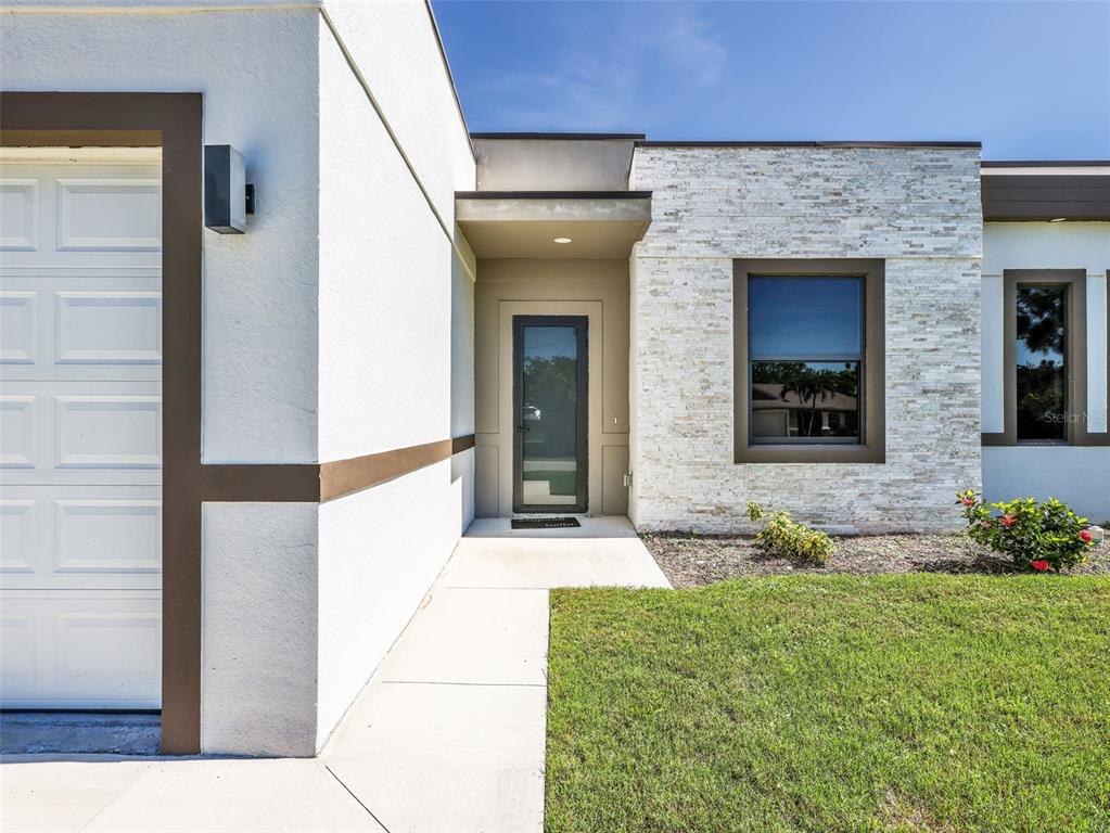 The exterior of a modern home features a white stucco wall, stone veneer, and entryway — 1423 NW 20TH TERRACE, CAPE CORAL, FL
