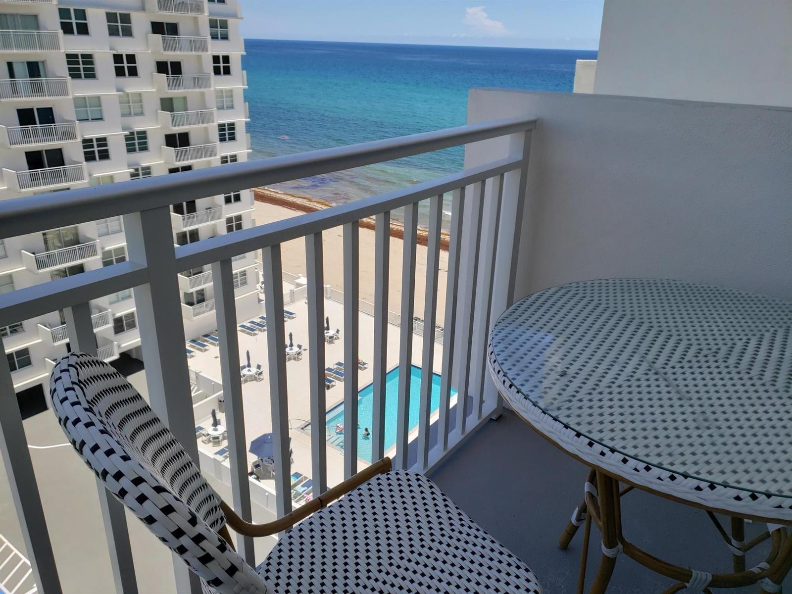 A balcony with a small table and chair overlooks a swimming pool, beach, and ocean — 4511 S Ocean Boulevard # 904, Highland Beach FL 33487, HIGHLAND BEACH, FL