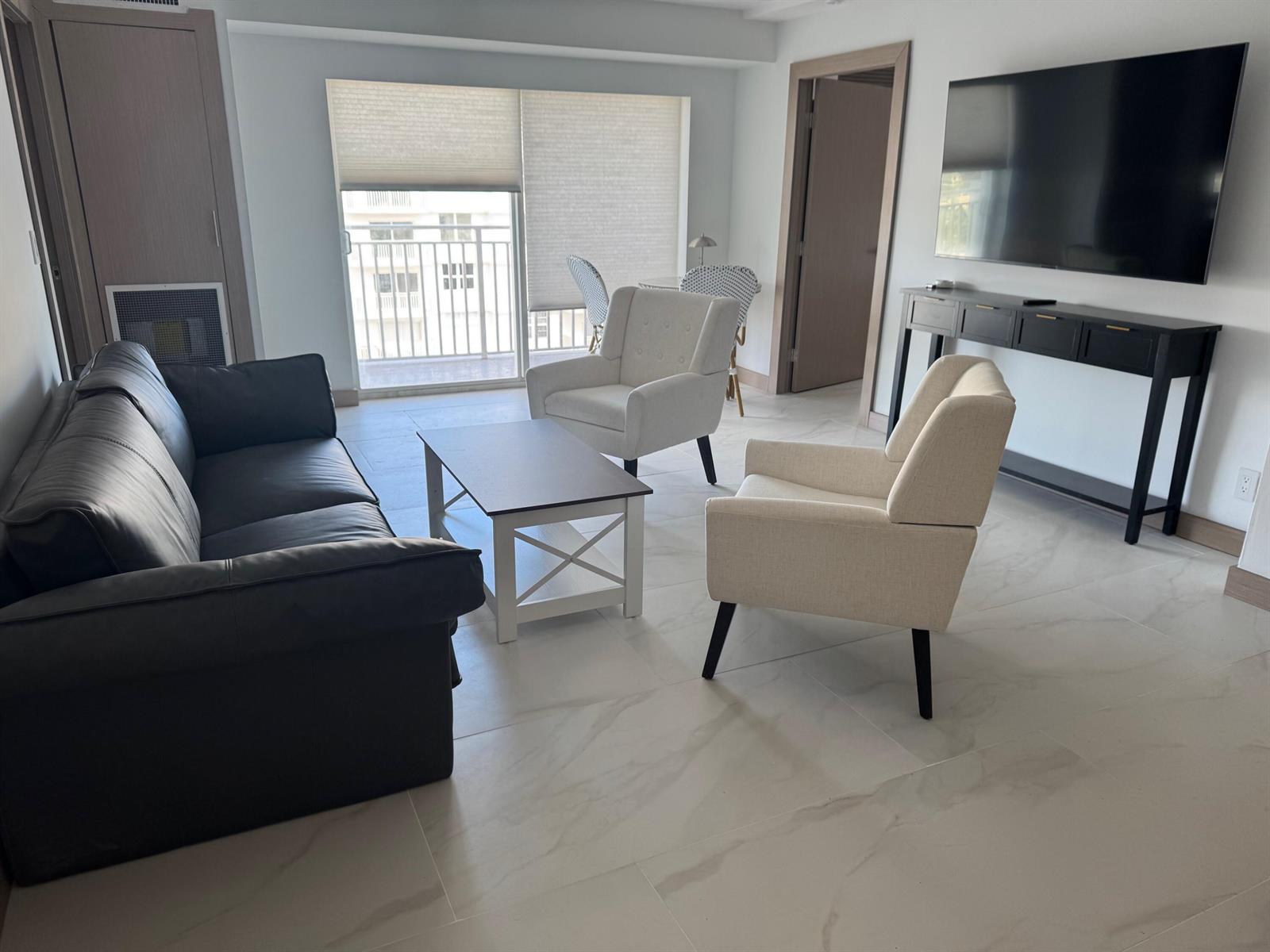 A living room features a dark sofa, two light armchairs, a coffee table, and a television — 4511 S Ocean Boulevard # 904, Highland Beach FL 33487, HIGHLAND BEACH, FL