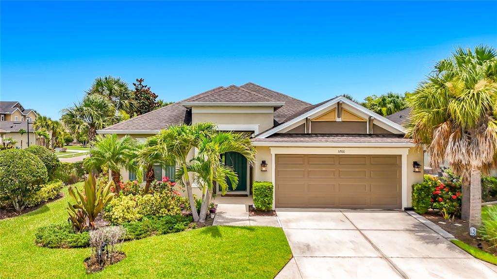 A single-story house with a tan exterior, a two-car garage, and palm trees in front — 5766 MAYPOP CIR, SARASOTA, FL