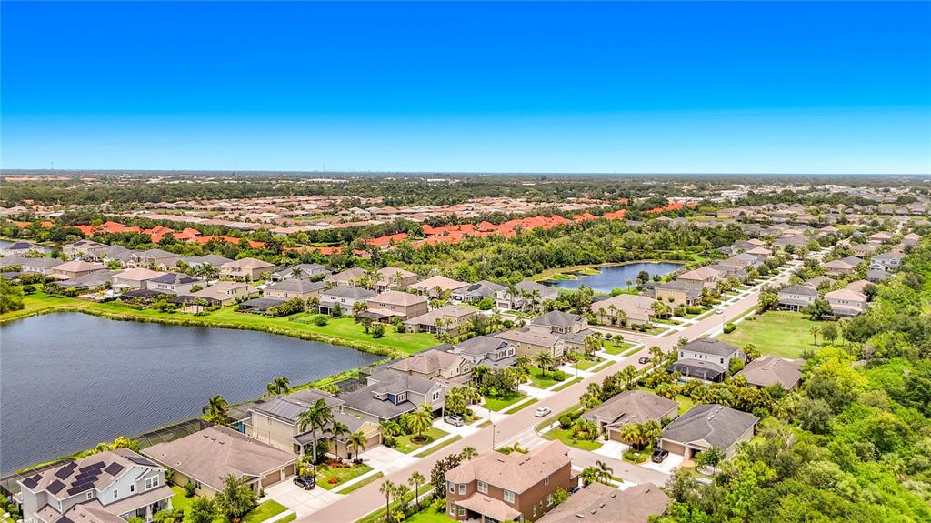 An aerial view shows a suburban neighborhood with houses, a lake, and surrounding greenery — 5766 MAYPOP CIR, SARASOTA, FL