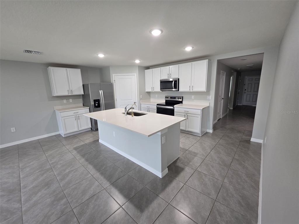 A modern kitchen features white cabinets, stainless steel appliances, a central island, and gray tile flooring — 4703 SW 85TH PLACE, OCALA, FL