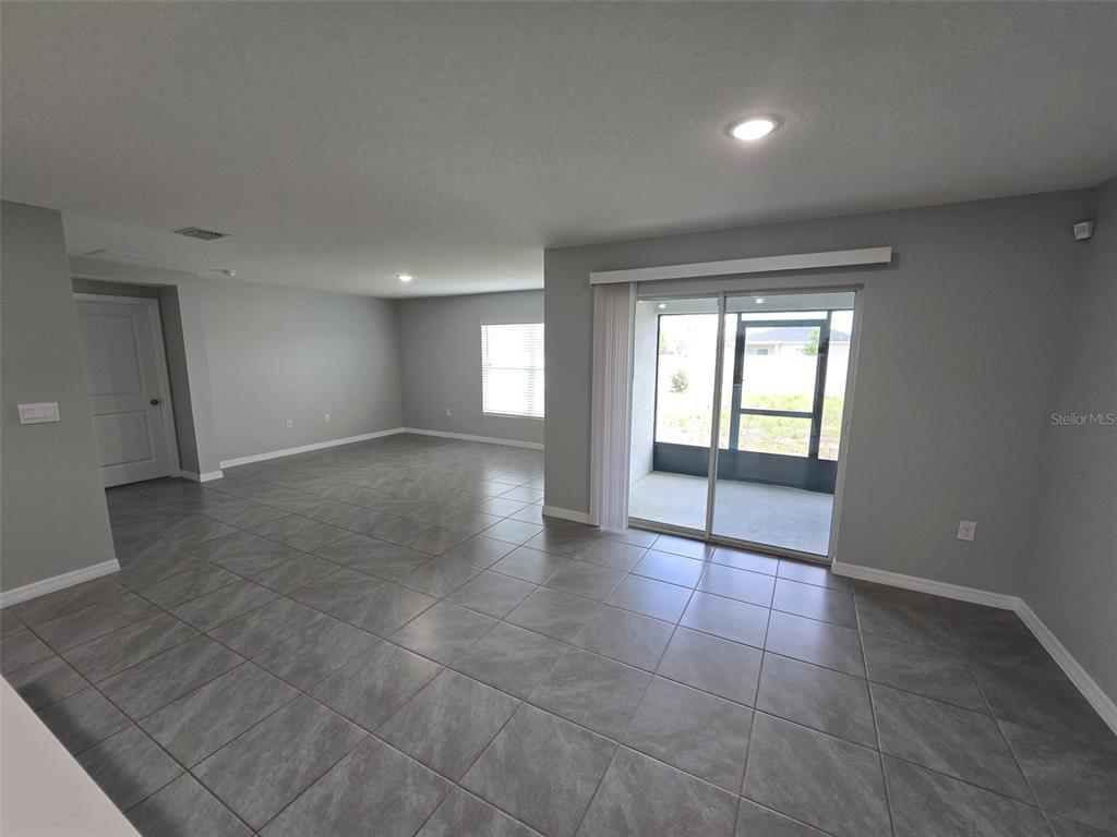 An open living area features gray tile flooring, light gray walls, and a sliding glass door — 4703 SW 85TH PLACE, OCALA, FL