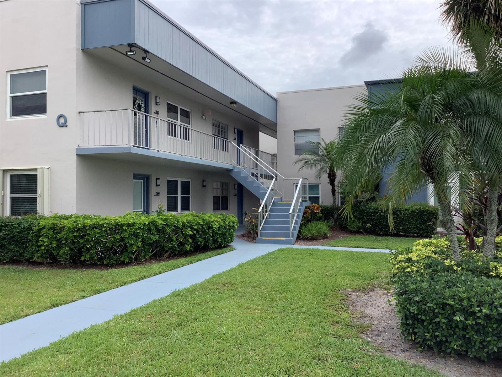 A two-story apartment building exterior features a blue staircase, balcony, and landscaped lawn — 794 Normandy Q, Delray Beach FL 33484, DELRAY BEACH, FL