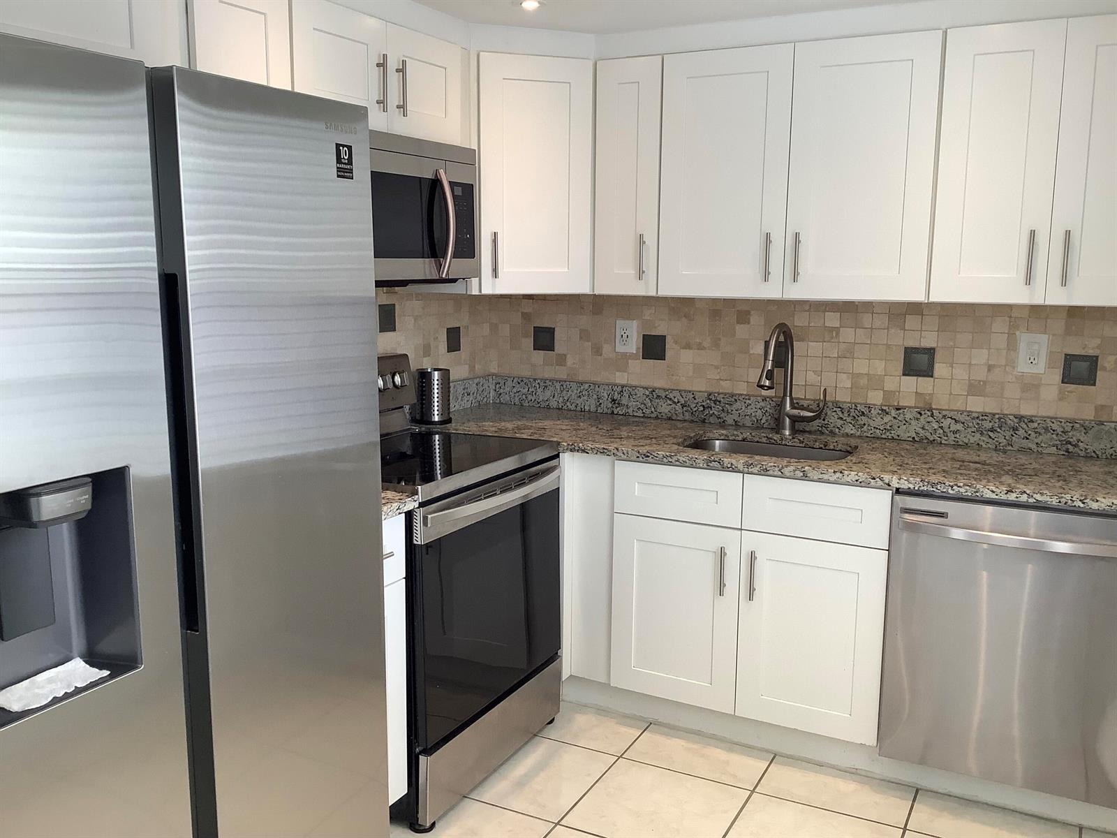 A kitchen features white cabinets, stainless steel appliances, granite countertops, and a tiled backsplash — 794 Normandy Q, Delray Beach FL 33484, DELRAY BEACH, FL