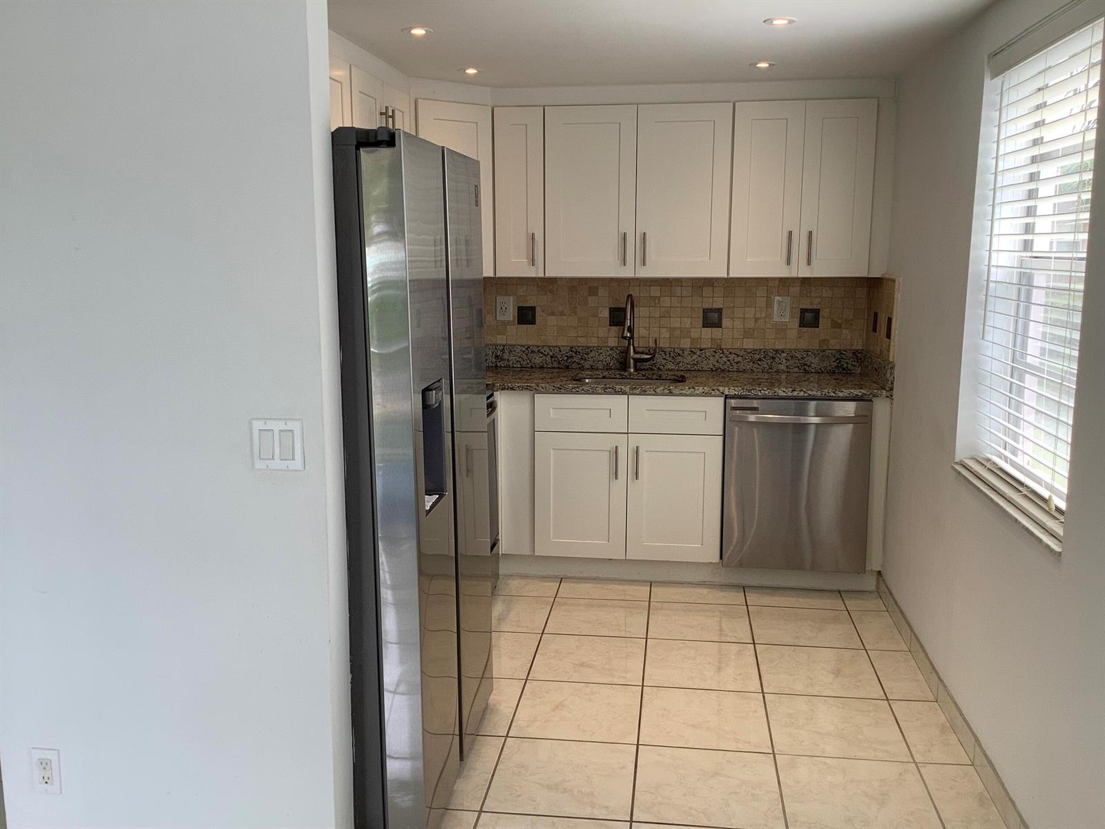 A kitchen features white cabinets, granite countertops, stainless steel appliances, and beige tile flooring — 794 Normandy Q, Delray Beach FL 33484, DELRAY BEACH, FL