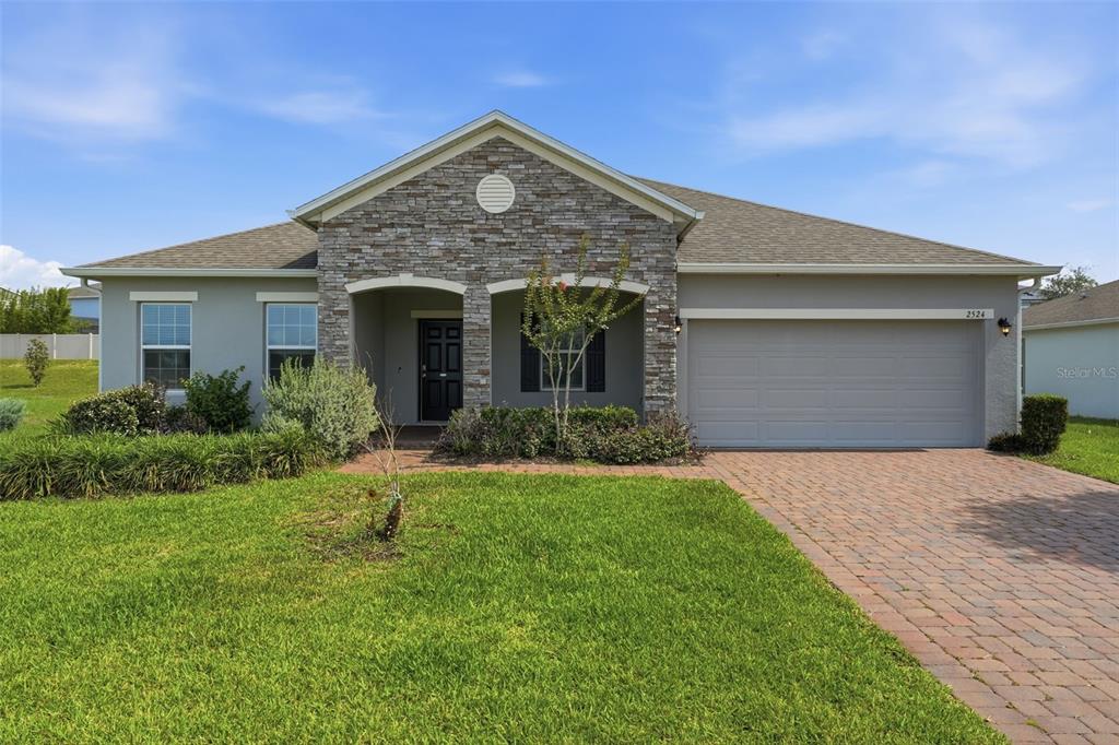 A single-story house features a stone facade, a two-car garage, and a brick paver driveway — 2524 CARRIAGE POINTE LOOP, APOPKA, FL