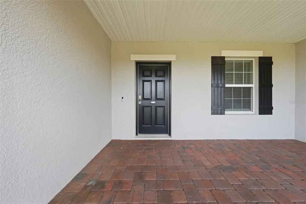 A covered front porch features a black door, a window with shutters, and brick pavers — 2524 CARRIAGE POINTE LOOP, APOPKA, FL