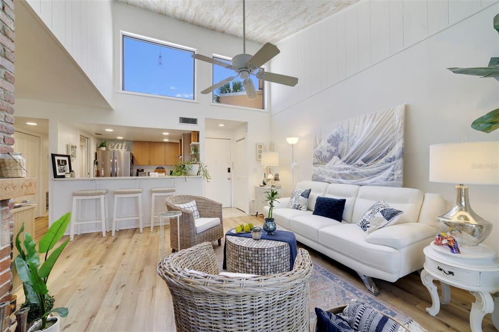 A bright living room with high ceilings, white walls, wicker furniture, and an open kitchen — 1051 S HIGHLAND STREET UNIT 7D, MOUNT DORA, FL