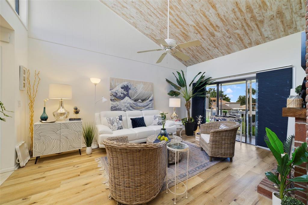 A living room features a vaulted wood-paneled ceiling, white sofa, wicker chairs, and sliding doors — 1051 S HIGHLAND STREET UNIT 7D, MOUNT DORA, FL
