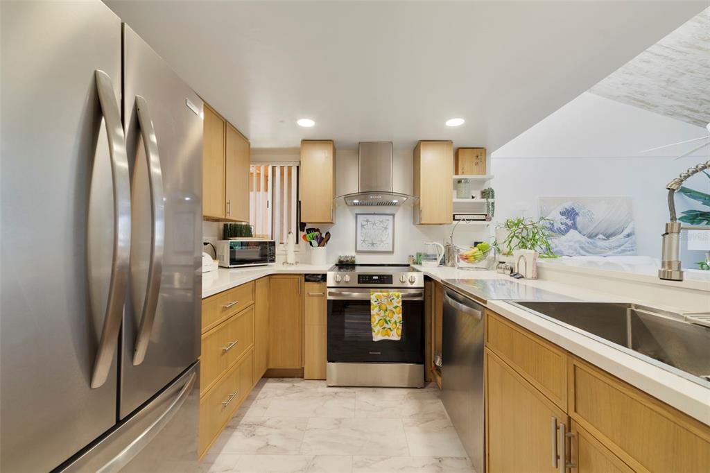 A galley kitchen features light wood cabinets, stainless steel appliances, and white marble-look flooring — 1051 S HIGHLAND STREET UNIT 7D, MOUNT DORA, FL