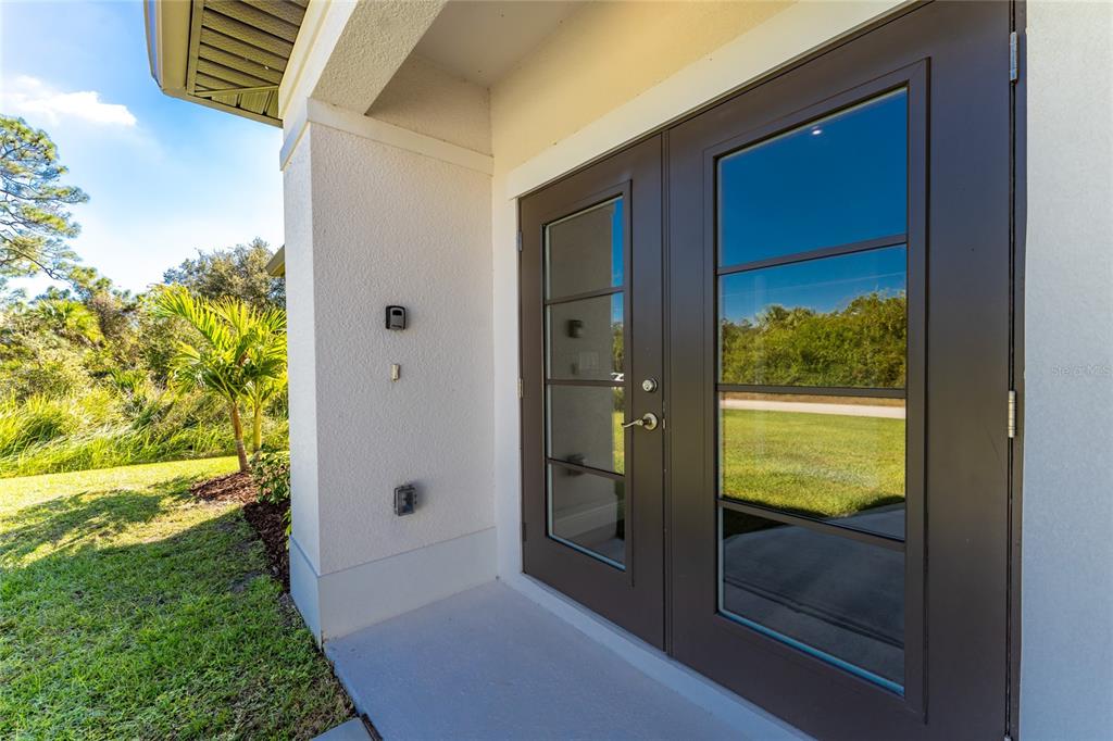 A set of dark-framed French doors opens onto a concrete patio beside a grassy yard — 6397 FILBERT STREET, NORTH PORT, FL